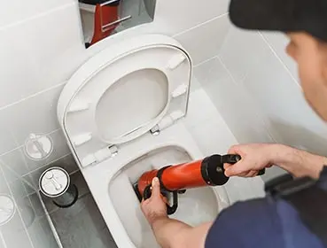 Plumber using a toilet auger to clear a clogged toilet, illustrating Bud's Plumbing & Repair Service's toilet repair expertise.