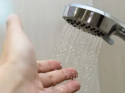 Hand reaching towards a showerhead with water droplets, illustrating issues with hot water supply related to water heater malfunction.