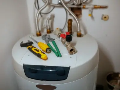 Water heater with tools including pliers, adjustable wrench, and screwdriver, indicating maintenance or repair needs related to aging or frequent repairs.
