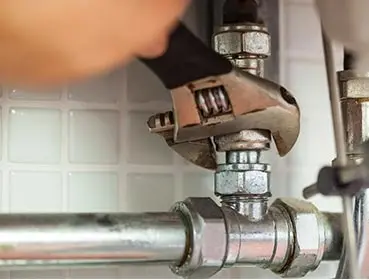 Plumber using adjustable wrench on plumbing fittings, showcasing repair services for residential plumbing needs.