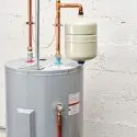 Gray water heater and white expansion tank with copper piping for plumbing by Bud's Plumbing.