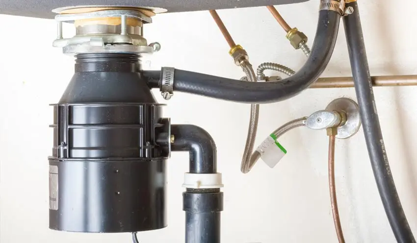 Garbage disposal unit installed under a kitchen sink, showcasing plumbing connections and components relevant to Bud's Plumbing & Repair Service's installation and repair services in Evansville, Indiana.