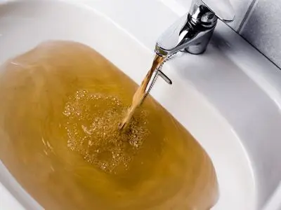 Discolored water flowing from a faucet into a sink, illustrating brown and rusty water issues caused by sediment buildup and corrosion in water heater tanks.