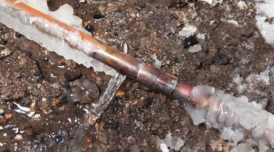 Frozen copper pipe with ice buildup and water leaking, illustrating plumbing issues related to winter conditions.