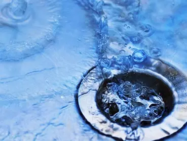 Water flowing into a drain, highlighting plumbing services related to drain cleaning and repairs offered by Bud's Plumbing & Repair Service.