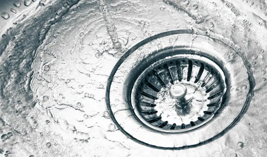 Close-up of a kitchen sink drain with water flowing down, illustrating the importance of professional drain cleaning services by Bud's Plumbing in Evansville, Indiana.