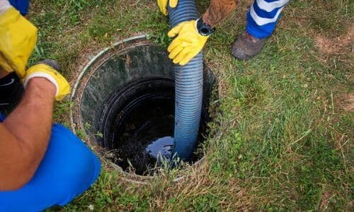 Technician using a hose to clear a clogged sewer main from a cleanout access point, emphasizing professional plumbing services for effective drain maintenance.