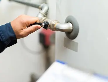 Hand adjusting a valve on a water heater, highlighting plumbing maintenance services offered by Bud's Plumbing & Repair Service in Evansville.