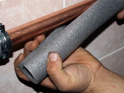 Hand applying foam insulation to a copper pipe, demonstrating effective pipe insulation techniques to prevent frozen pipes during winter.