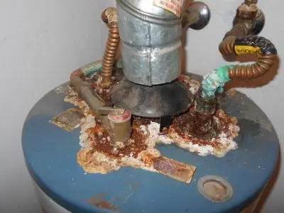 Corroded water heater tank showing significant rust and mineral buildup around connections, indicating potential need for replacement.