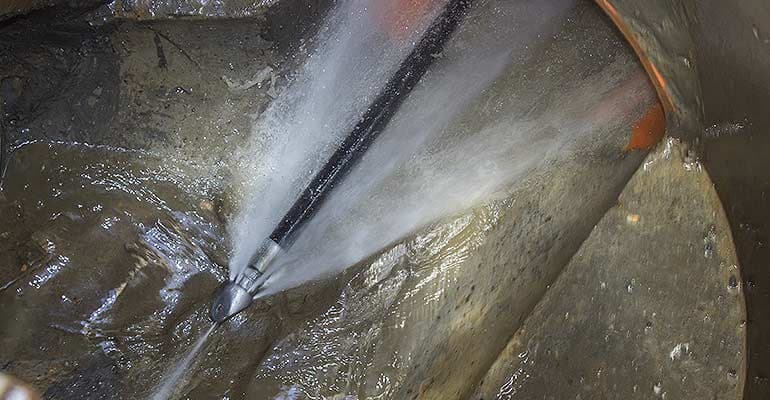 Hydrojetting service in action, high-pressure water jet clearing stubborn drain clogs in plumbing system.