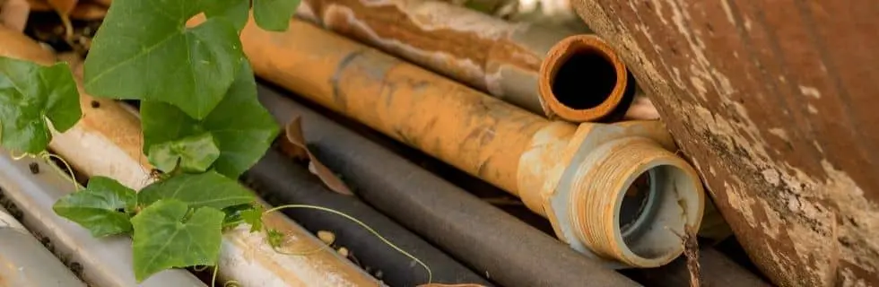 Corroded and damaged plumbing pipes surrounded by greenery, highlighting issues of pipe maintenance and corrosion in home plumbing systems.