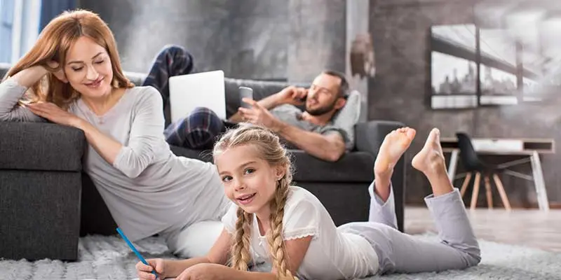 Family enjoying indoor activities in a modern living room, focusing on air quality and comfort, with a mother and daughter drawing while a father uses a smartphone.