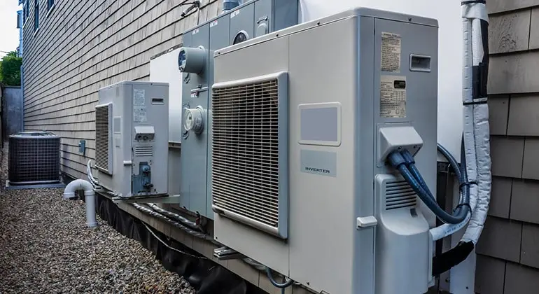 Air conditioning units and heating systems installed on a gravel surface outside a building, showcasing energy-efficient HVAC technology.