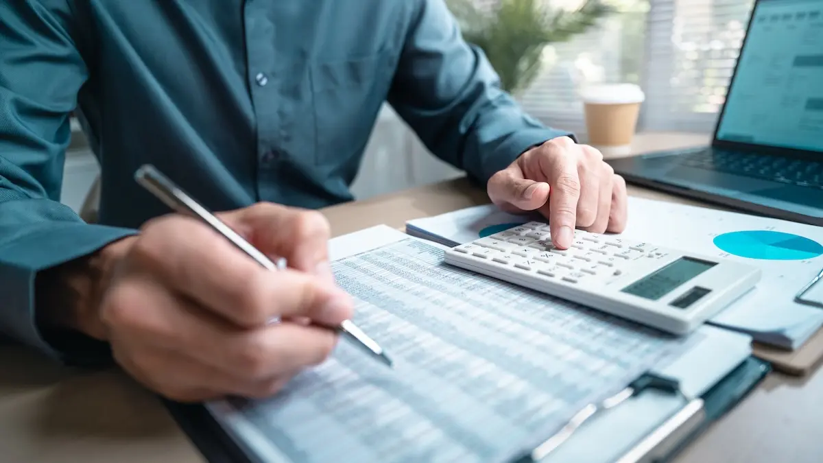 Person using calculator and reviewing financial documents for accounting and budget planning.