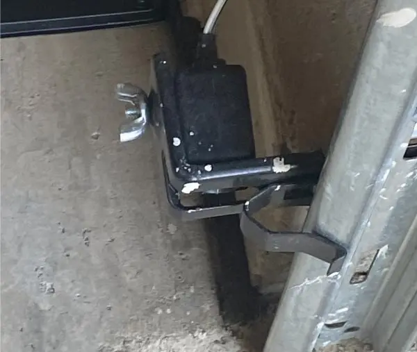 Close-up image showing a homeowner cleaning the dust and grime off the lens of a malfunctioning garage door safety sensor.