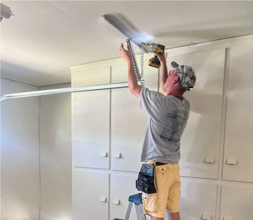 Technician in a brown and orange uniform performing a garage door repair in Dinuba, CA