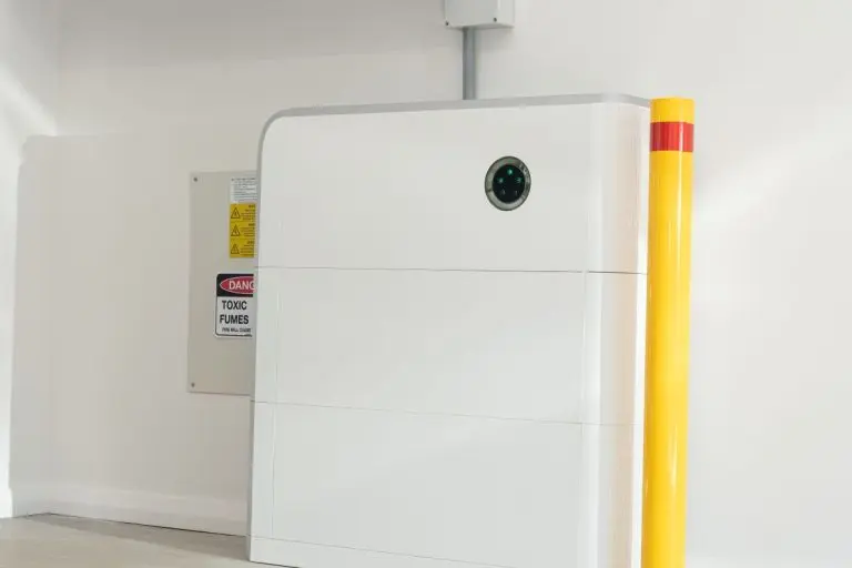 Solar battery home storage unit in a garage with yellow safety bollard and warning signs
