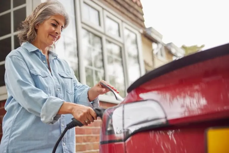 Woman Attaching Charging Cable To Environmentally Friendly Zero Emission Electric Car At Home