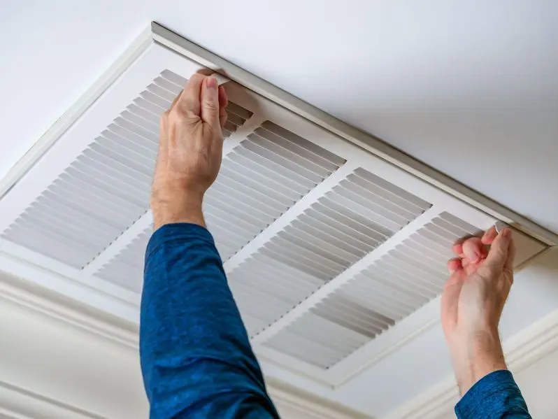 Man opening ceiling air vent to replace dirty HVAC air filter.