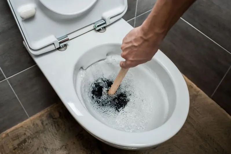 cropped view of plumber using plunger in toilet bowl during flushing in modern restroom with grey tile