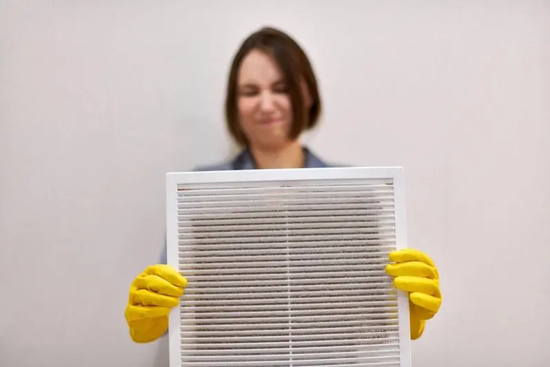 Woman holds ventilation grill with dust filter to clean it