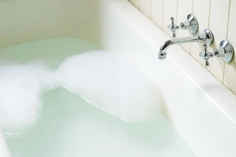 Old bath tub with bubbles, water and hot and cold tap