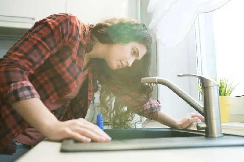 young woman checking faucet while having problem with dropping faucet in kitchen