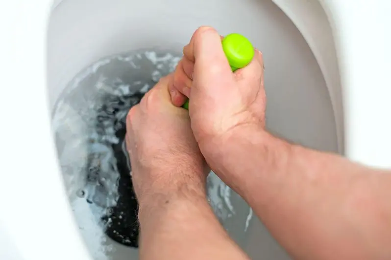 Plumber repairing toilet with hand plunger.