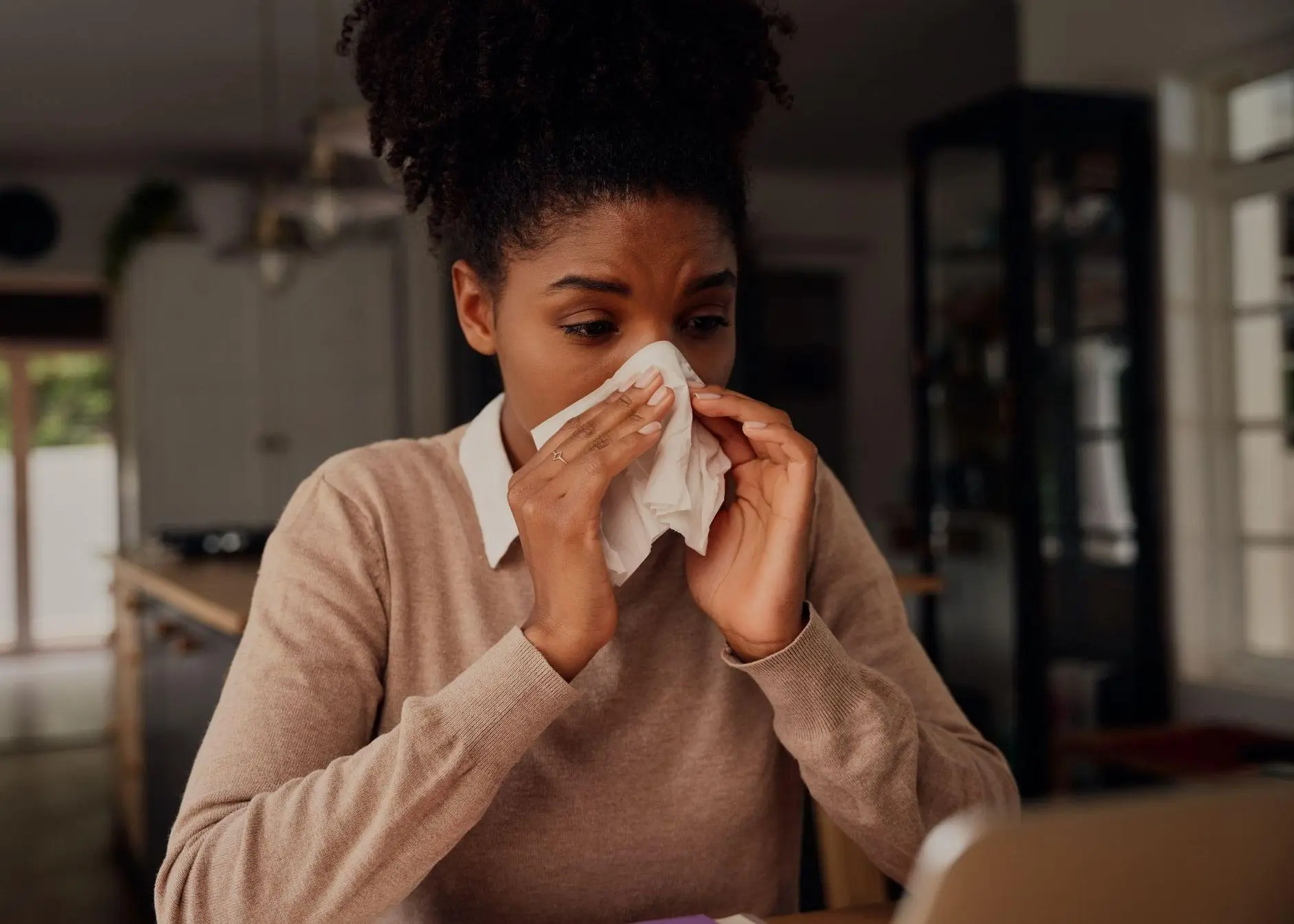 Sick woman blowing nose in tissue paper while sitting at home