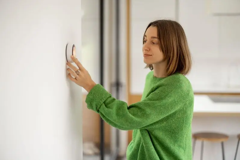 Woman controlling temperature with a smart thermostat mounted on the wall at modern apartment.