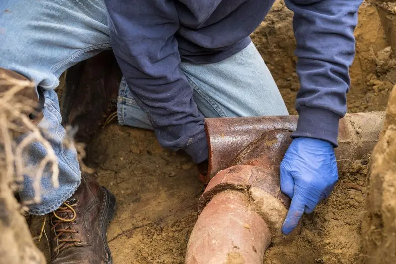 man digging tree roots out of an old ceramic sewer pipe in a hole