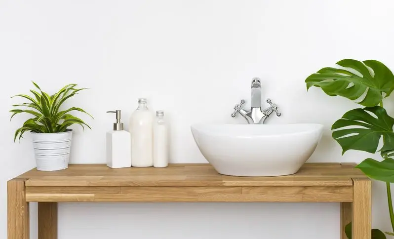 Bathroom wooden table with washbasin, faucet, plants and soap bottles