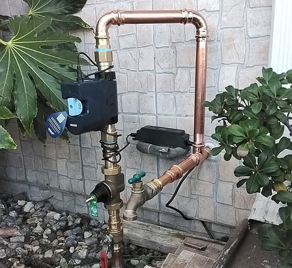 Copper plumbing system with a digital water meter, surrounded by greenery, illustrating advanced plumbing solutions for home maintenance in Long Beach, CA.