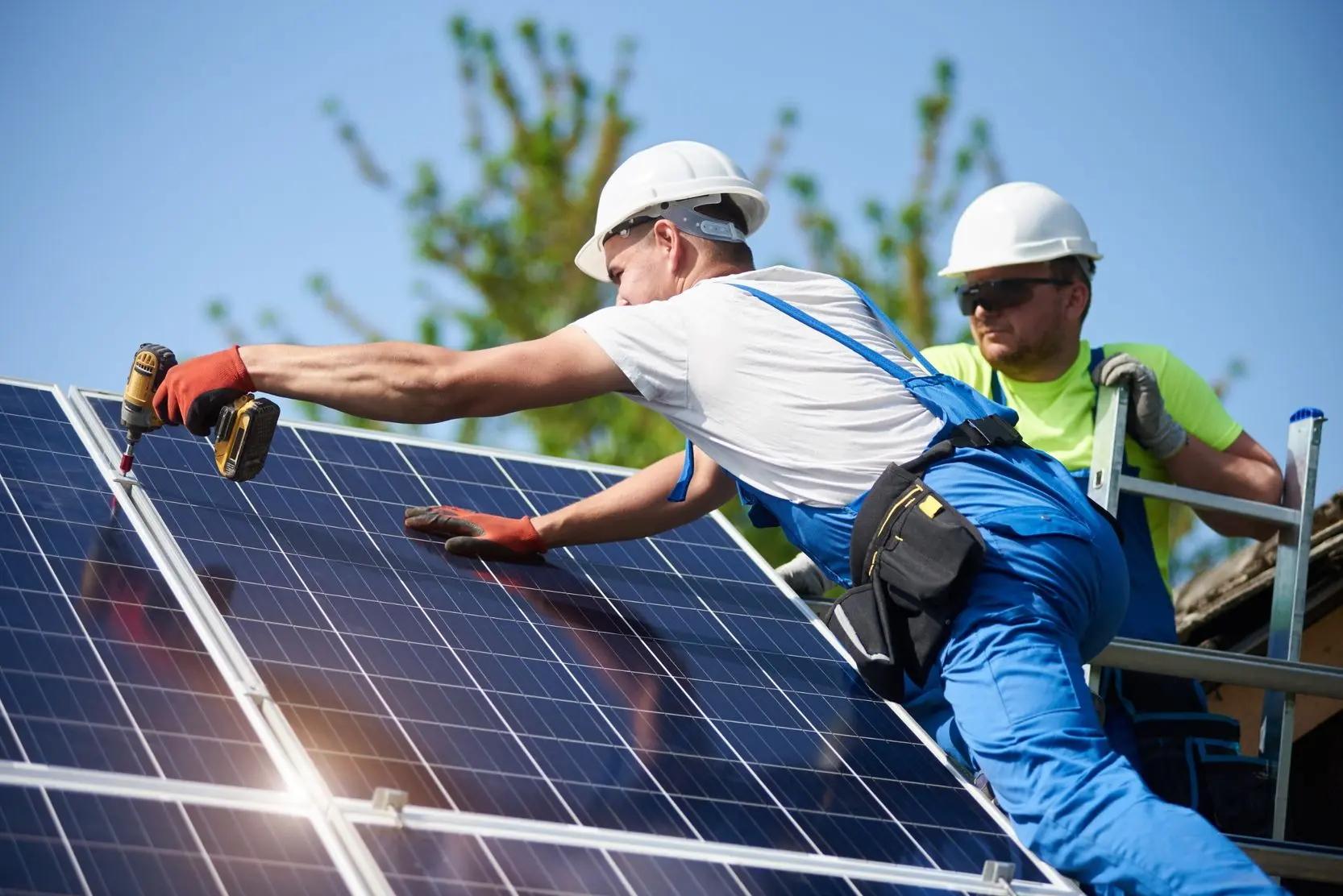 Two solar panel technicians on a roof install a solar panel using a drill.