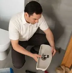 Plumber kneeling and inspecting a sink fixture in a bathroom, demonstrating professional plumbing services in Springfield, NE.