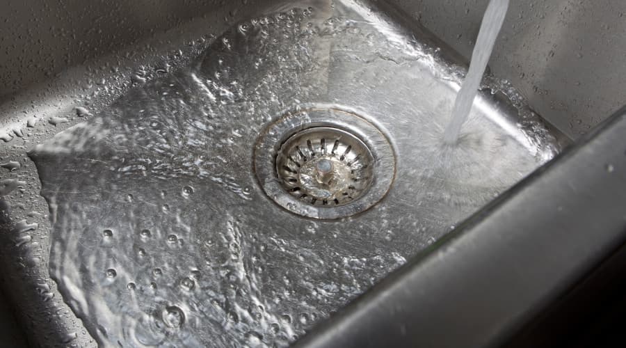 Water flowing into a stainless steel sink with visible ripples around the drain, illustrating the importance of drain cleaning and plumbing maintenance.