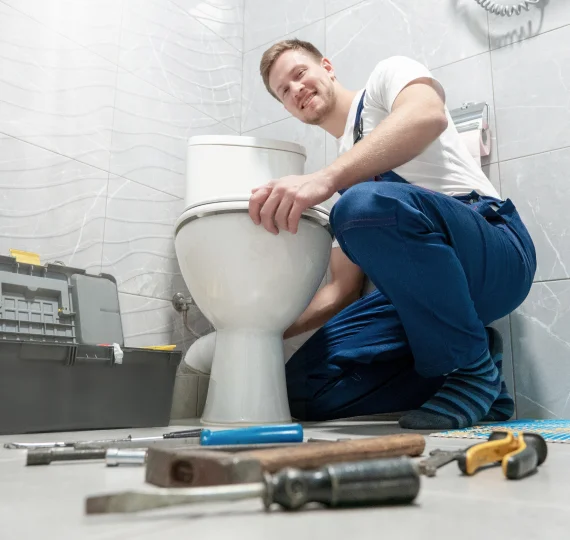 Plumber installing a toilet in a bathroom, surrounded by tools, emphasizing professional toilet installation services in Maryland.