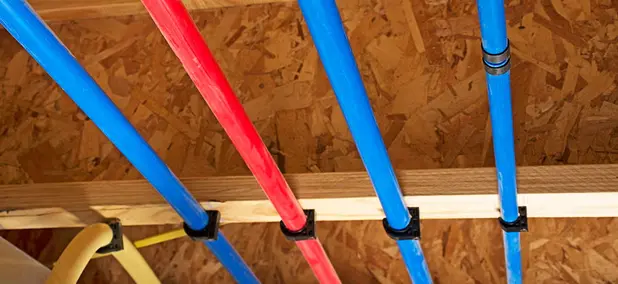 Colorful repiping installation with red and blue pipes in a wooden framework, illustrating whole house repiping services by Florida Plumbing Plus.