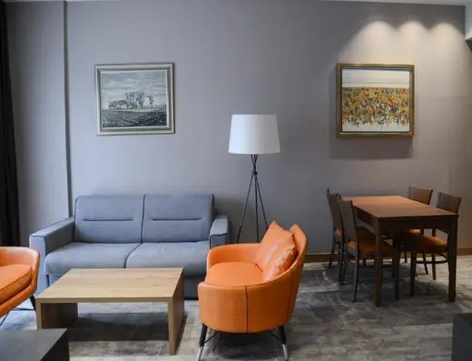 Dnevna soba apartmana u Mövenpick Resort & Spa Fruške Terme sa sivim kaučem, narandžastim foteljama, drvenim stolom za ručavanje i umetničkim slikama na zidu