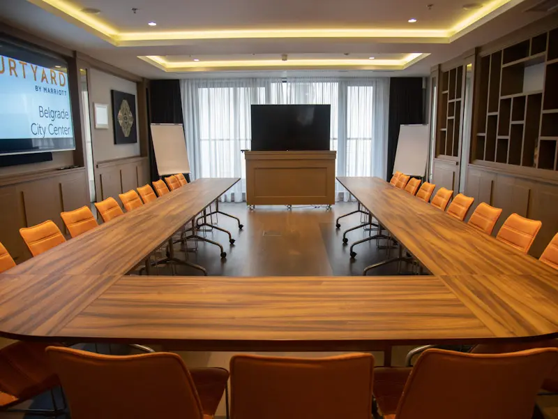 Velika konferencijska sala u hotelu Courtyard Belgrade City Center sa boardroom rasporedom, narandžastim stolicama, velikim TV ekranom i projektorskim platnom