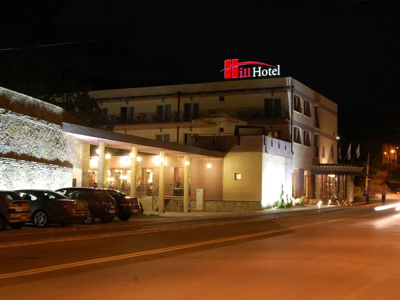 Eksterijer Hill Hotel sa kamenom fasadom, svetlećim natpisom, stubovima i osvetljenim ulazom noću