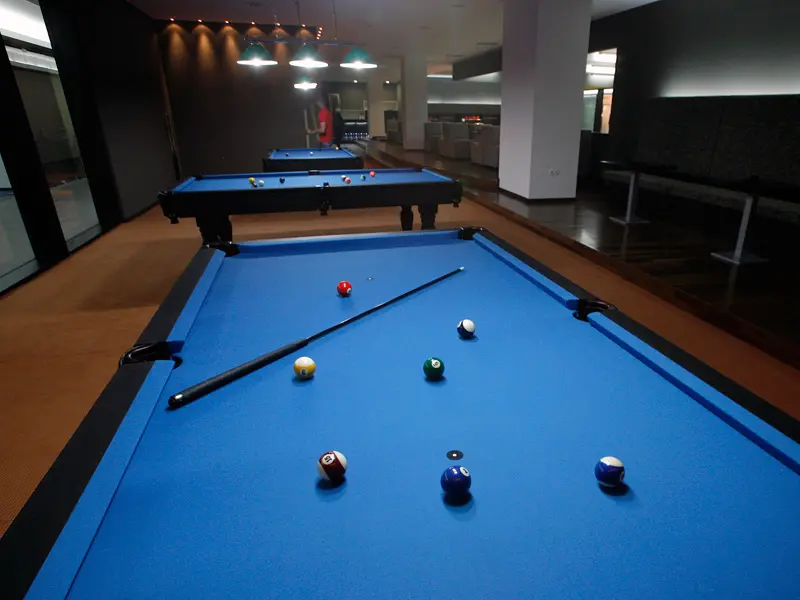 Bilijar sala u Radon Plaza Hotel sa plavim bilijar stolovima, štapovima, šarenim kuglama i ambijentalnim osvetljenjem