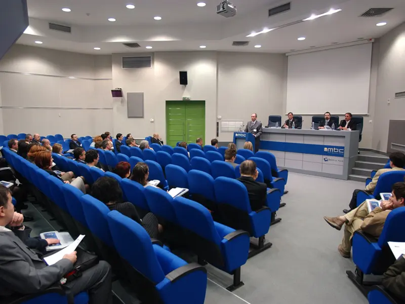 Auditorijum u ERA Group Skopje Fair Congress Center tokom konferencije sa panelistima za MBC stolom, plavim foteljama i publikom