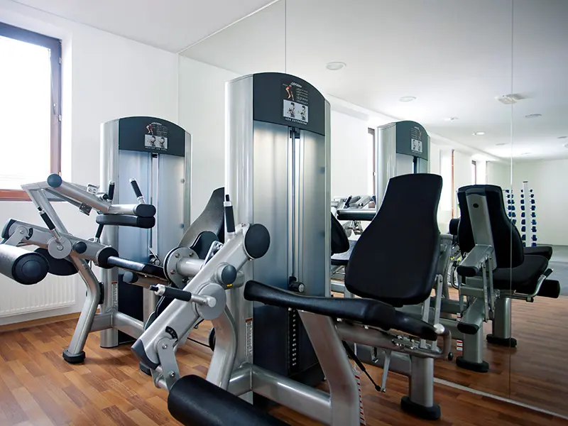 Fitnes sala u Hotel Palisad sa spravama za vežbanje nogu, ogledalom i drvenim podom