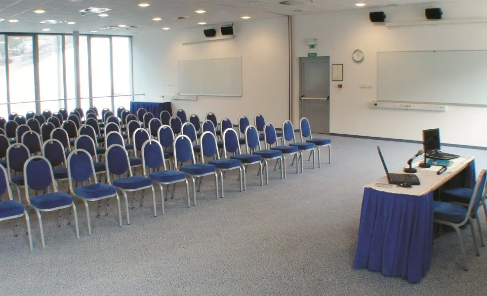 Konferencijska sala u Ramada Resort Kranjska Gora hotelu sa plavim stolicama u teatar rasporedu, projektorom i bijelim tablama