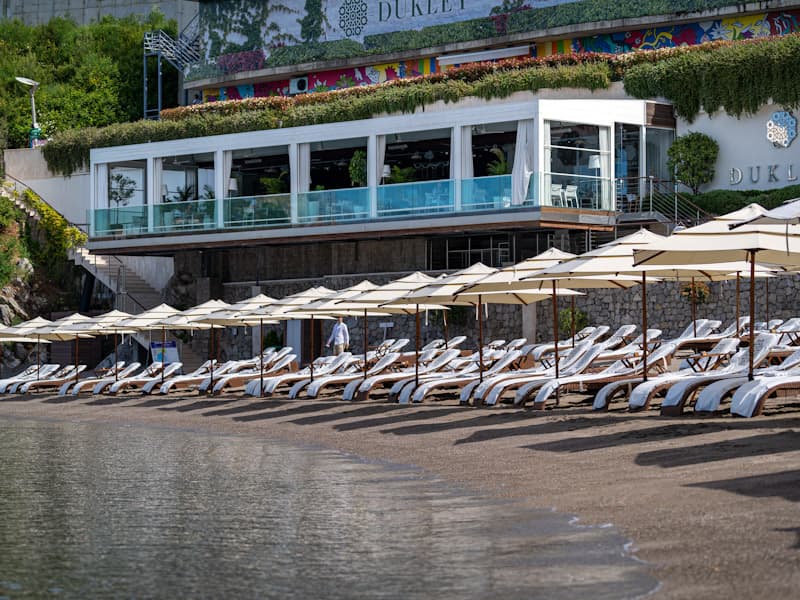 Plaža ispred Dukley Seafront Restaurant and Beach sa belim ležaljkama, suncobranima, staklenom terasom restorana i natpisom Dukley