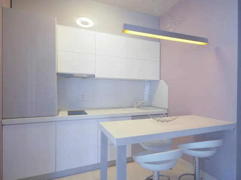 Kuhinja apartmana u Tre Canne hotelu sa belim elementima, barskim pultom, belim stolicama i toplim osvetljenjem