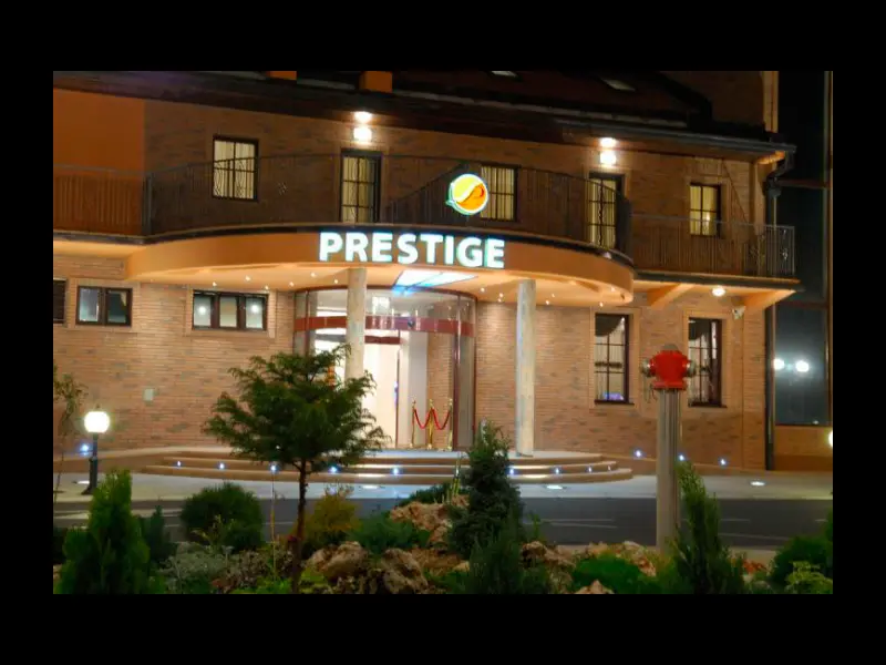 Eksterijer Hotel Prestige Beograd noću sa ciglenom fasadom, osvetljenim natpisom Prestige, fontanom i zelenim pejzažom