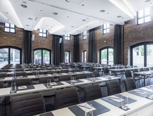 Velika konferencijska sala u hotelu Radisson Collection Hotel Old Mill Belgrade sa belim stolovima u učioničkom rasporedu, sivim stolicama, ciglenim zidovima i lučnim prozorima